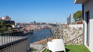 A balcony with a view of a bridge, a white chair, and a building with a tree. - E: Sweeping Panoramic Terrace | Douro Views (Vila Nova de Gaia)