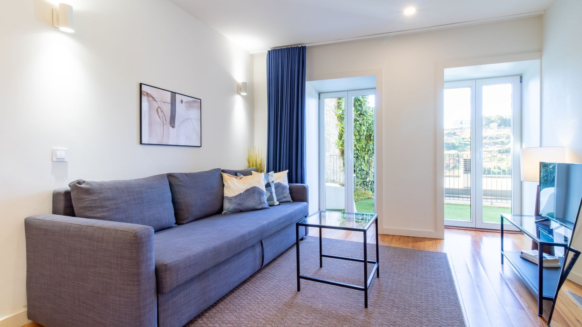 Ein modernes Wohnzimmer mit grauem Sofa, einem Glastisch und Blick auf einen Balkon.