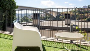 A balcony with a white chair and a round table, overlooking a parking area and a bridge. - E: Sweeping Panoramic Terrace | Douro Views (Vila Nova de Gaia)
