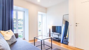 Uma sala de estar moderna com um sofá, uma mesa de centro de vidro, uma TV de tela plana e uma varanda com cortinas.