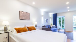 Quarto de hotel com uma cama grande, duas mesas de cabeceira com luminárias, um sofá e vista para o verde pela janela.