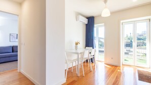 A modern living room with a sofa, a dining area with a table and chairs, and a large sliding glass door leading to a balcony with a view. - E: Sweeping Panoramic Terrace | Douro Views (Vila Nova de Gaia)