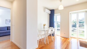 Uma sala moderna com um sofá, um espaço de jantar com mesa e cadeiras, e um grande painel de vidro deslizante que dá para uma varanda com vista.