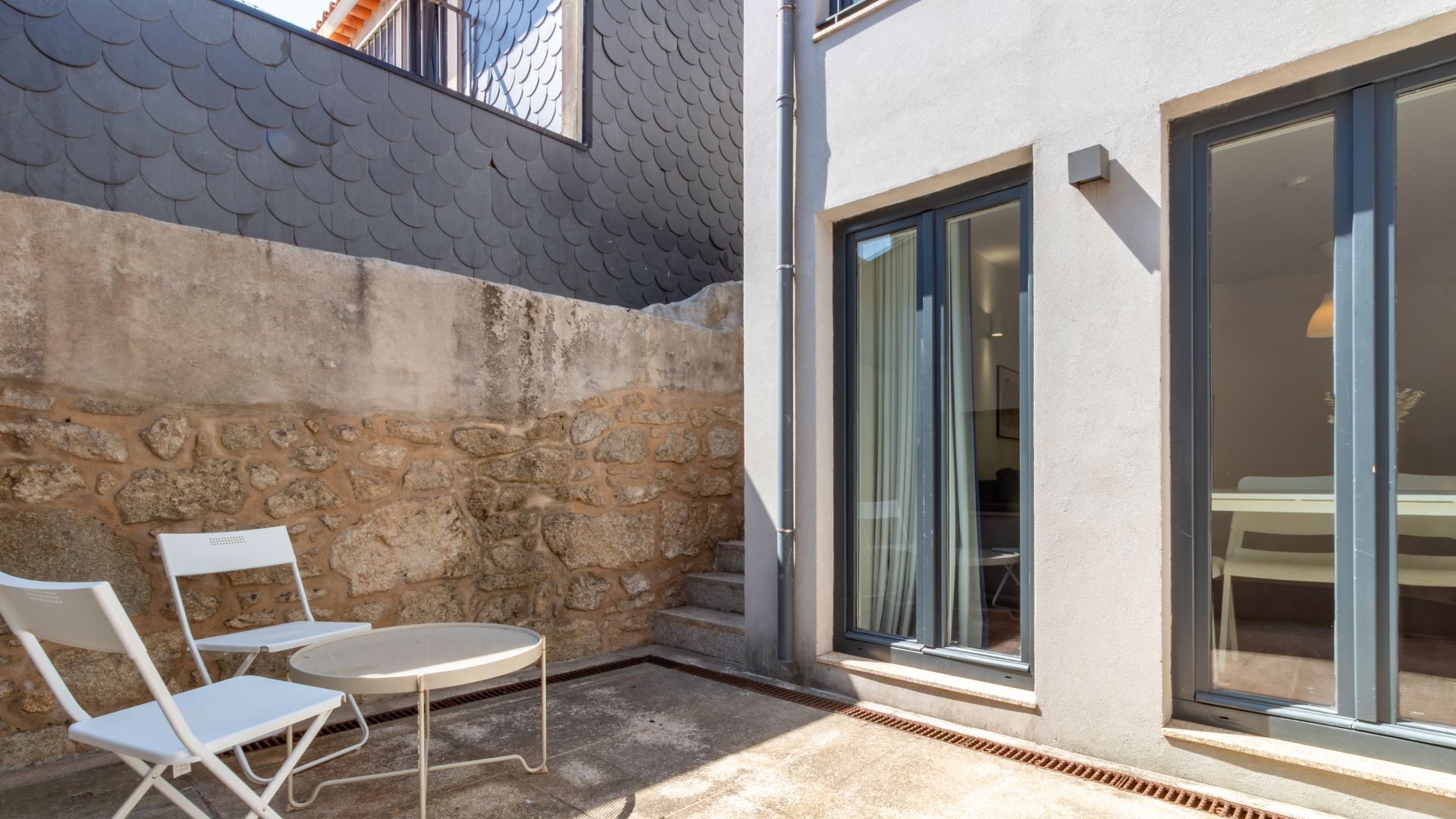 A patio area with a stone wall, a round table, two chairs, and a sliding glass door leading to an interior space.
