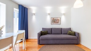 A modern living room with a grey sofa, a dining table, and a blue curtain. - H: Douro & Bridge Views | Boutique Apartments (Vila Nova de Gaia)
