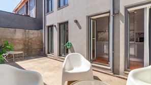 Eine Terrassensitzgruppe im Freien, ein grüner Gartenschlauch und ein Gebäude mit Steinwand und Schiebeglastüren.