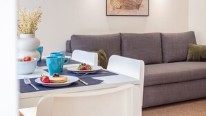 Ein Essbereich mit einem Tisch für zwei Personen, einem grauen Sofa und einer Vase mit Trockenblumen.