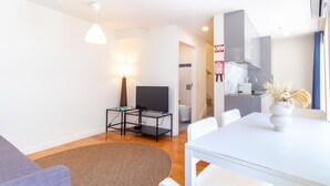 Ein modernes Wohnzimmer mit Sofa, Esstisch, Fernseher und Küchenzeile mit Spüle und Schränken.