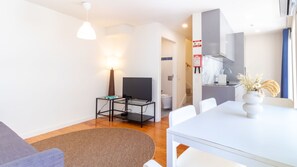 A modern living room with a sofa, a dining table, a TV, and a kitchen area with a sink and cabinets. - H: Douro & Bridge Views | Boutique Apartments (Vila Nova de Gaia)