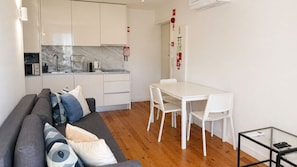 A compact living space with a kitchenette, a dining area, and a sofa with patterned cushions. - J: Iconic Bridge & Douro Views | 1BR Porto (Vila Nova de Gaia)