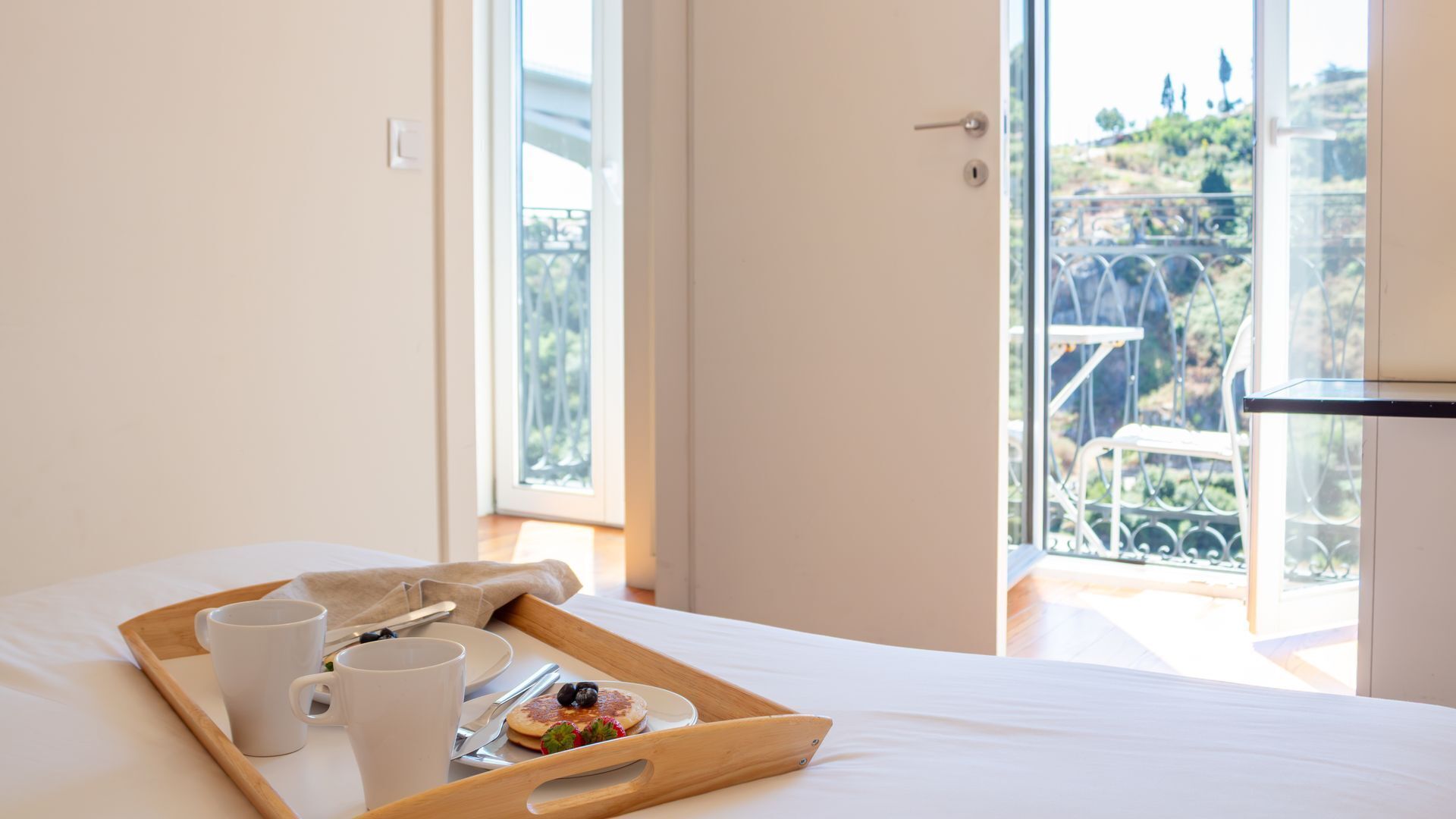 A hotel room with a bed, a tray with breakfast items, and a balcony with a view.