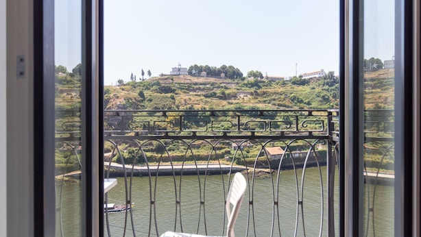 A view through a window with a metal railing, a river, and a hilly landscape with buildings in the distance. - M: Douro & Bridge Views | Sunny Porto Flat (Vila Nova de Gaia)