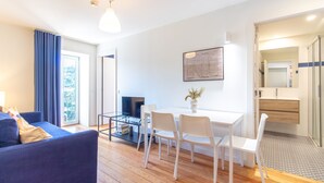 A modern living room with a sofa, a TV, a dining table with chairs, and a kitchen area visible through an open door. - M: Douro & Bridge Views | Sunny Porto Flat (Vila Nova de Gaia)