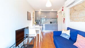 A modern kitchen with a marble backsplash, a dining area with a glass table, and a blue sofa with cushions. - M: Douro & Bridge Views | Sunny Porto Flat (Vila Nova de Gaia)