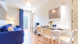 A modern living room with a blue sofa, a dining table with chairs, and a large window with curtains. - M: Douro & Bridge Views | Sunny Porto Flat (Vila Nova de Gaia)