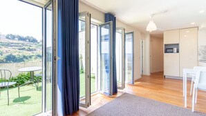 Eine moderne Wohnung mit großen Schiebeglastüren, einem Essbereich, einer Küche und Blick auf eine grüne Landschaft.