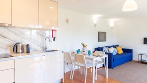 Eine moderne Küche mit Marmorarbeitsplatte, einem Wasserkocher und einer Kaffeemaschine. Es gibt einen Essbereich mit Tisch und Stühlen, und ein blaues Sofa im Wohnzimmer.