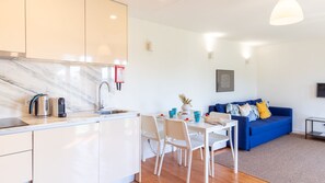 A modern kitchen with a marble countertop, a kettle, and a coffee machine. There is a dining area with a table and chairs, and a blue sofa in the living room. - N: Secret Garden & Douro Views | Peaceful Porto (Vila Nova de Gaia)