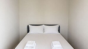 A single bed with white linens, a grey headboard, and two folded white towels at the foot of the bed. - O: Douro & Bridge Views | Boutique Apartments (Vila Nova de Gaia)