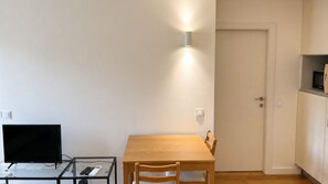 A small room with a wooden table, a glass table with a TV and remote controls, a wall-mounted light, and a door. - O: Douro & Bridge Views | Boutique Apartments (Vila Nova de Gaia)