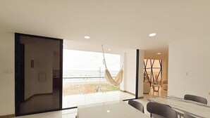 A modern hotel room with a large window, a dining area with a table and chairs, and a hammock. - Beach Front entire Private Building 32+ PAX (Montanita)