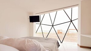 A bedroom with a bed, a TV mounted on the wall, and a large window with a geometric pattern. - Beach Front entire Private Building 32+ PAX (Montanita)