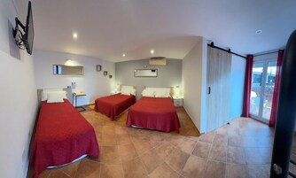 A hotel room with three beds, a desk, a chair, and a sliding glass door leading to a balcony.