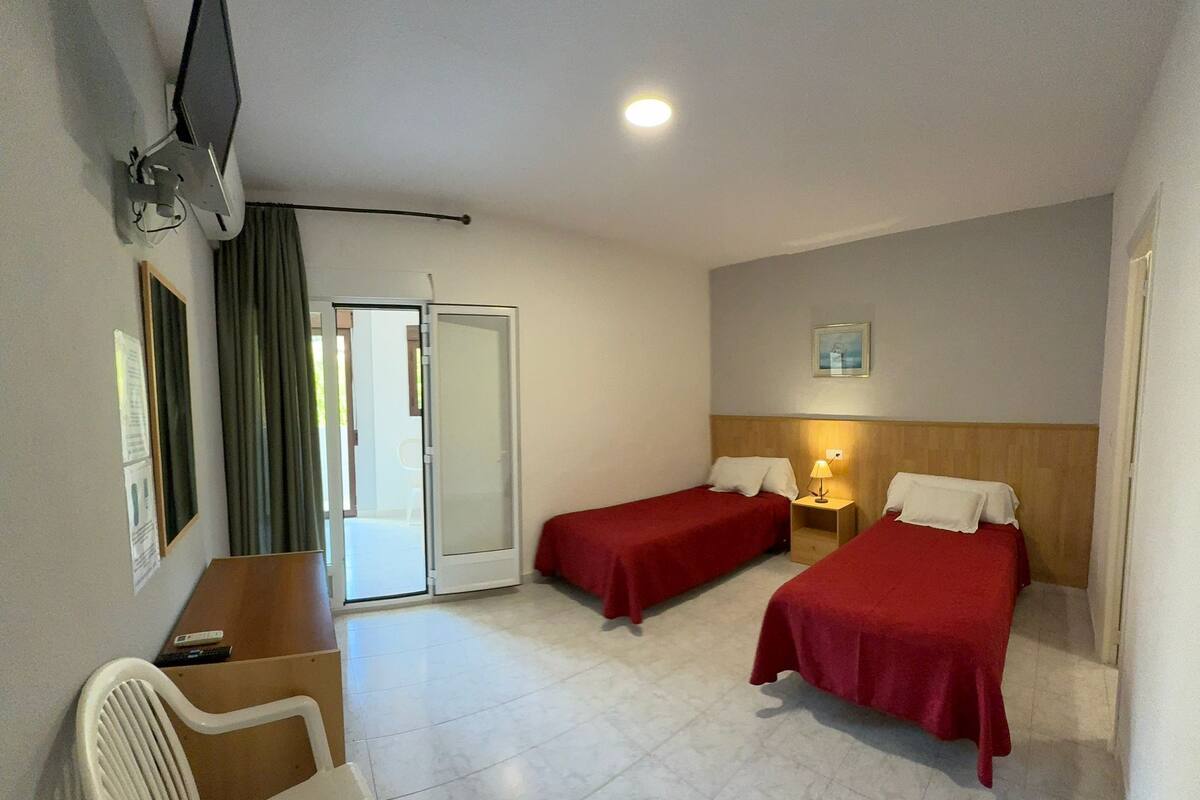 A hotel room with two single beds, a desk with a chair, a television, and a sliding door to the outside.