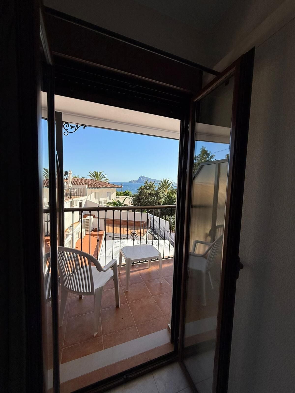 Varanda com vista para a costa, cadeiras brancas e uma mesa.