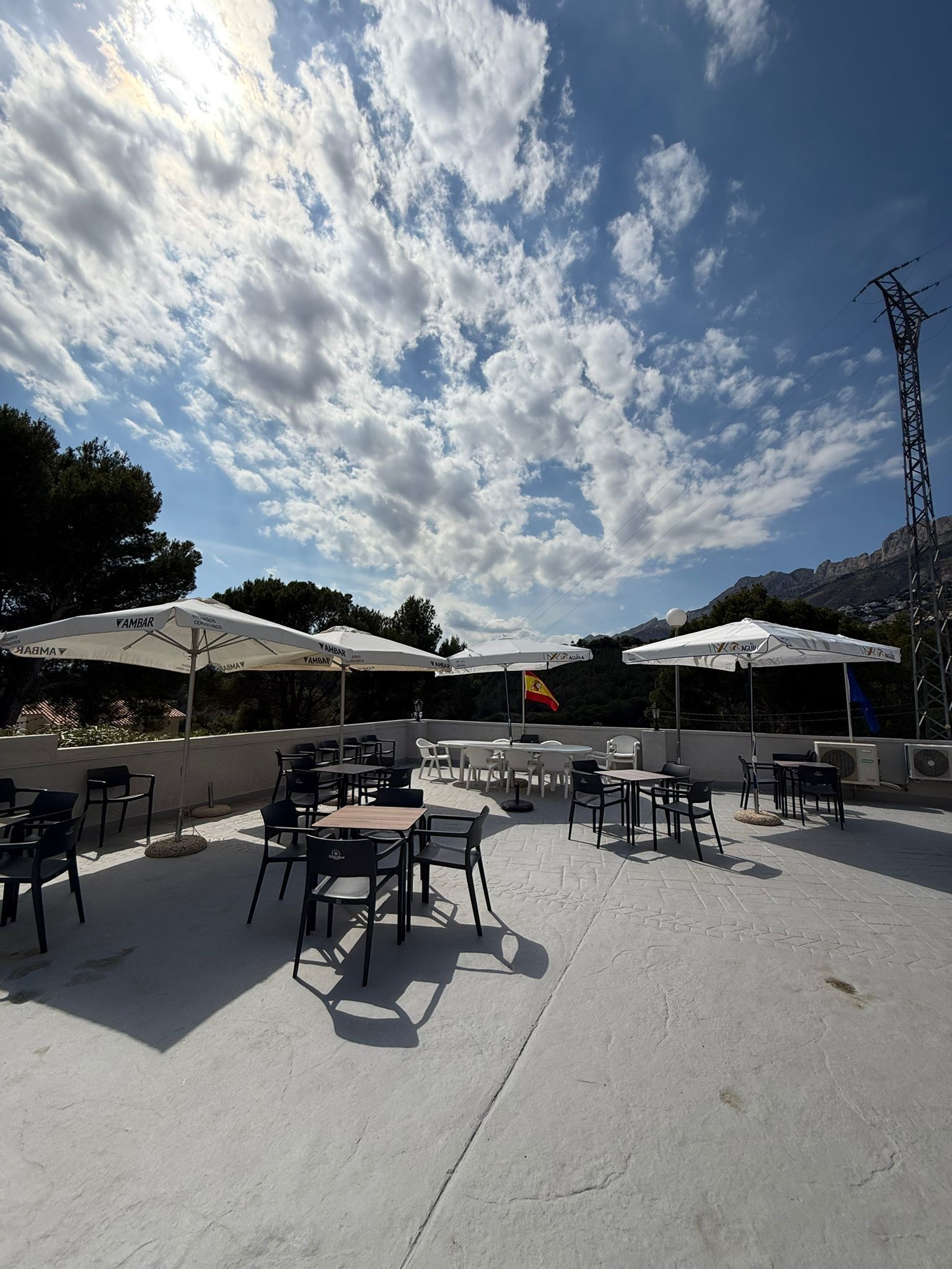 An outdoor patio with tables and chairs, umbrellas, and a flag.