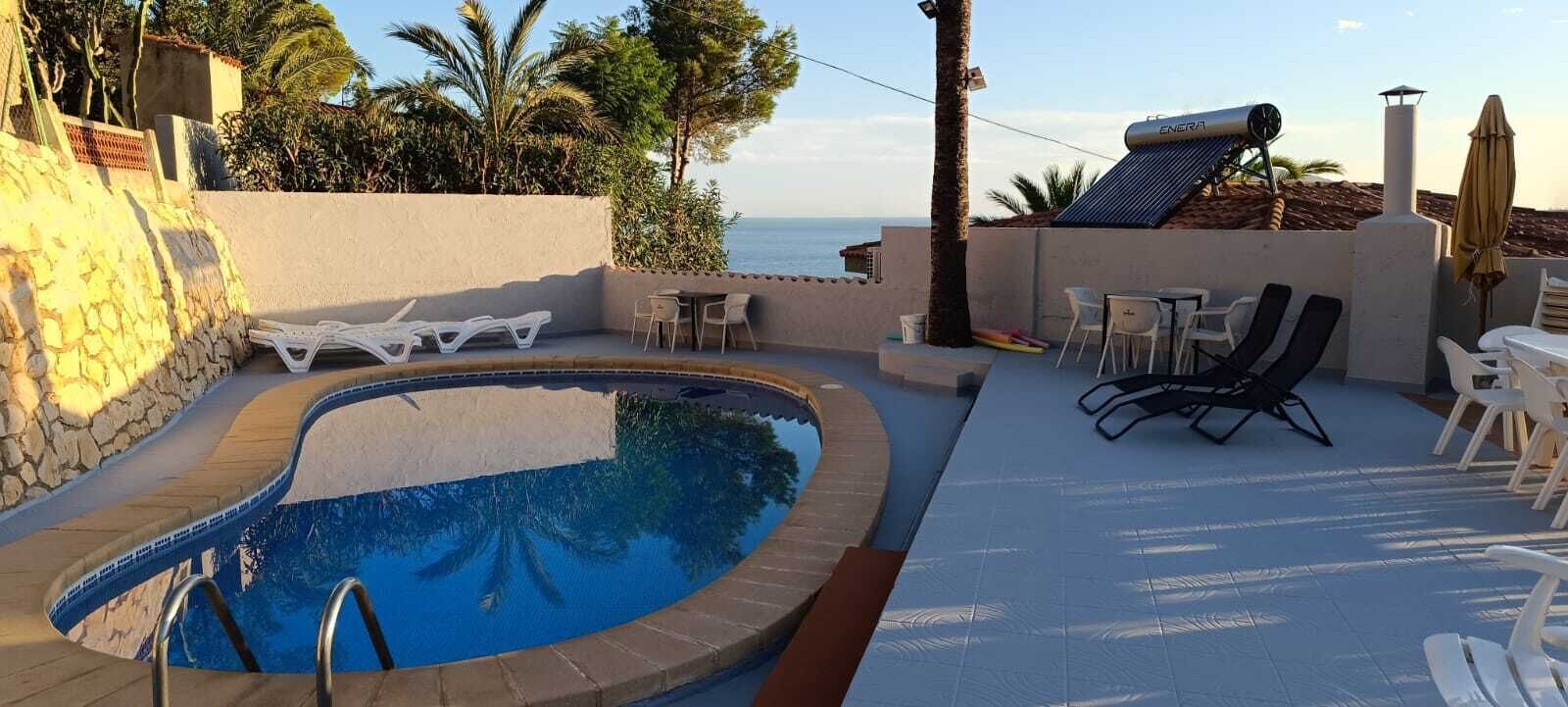 Une piscine avec des chaises longues et des tables, une vue sur la mer et un système de chauffage solaire de l’eau.