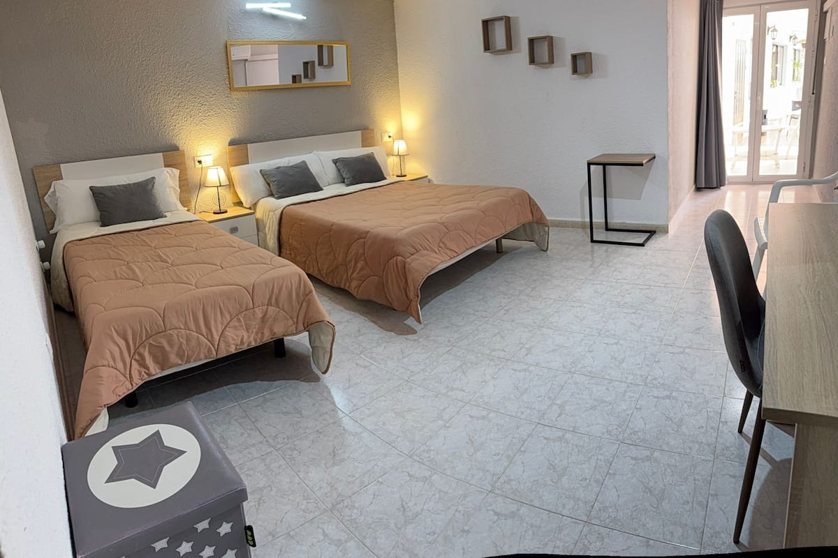 A hotel room with two beds, a desk, a chair, and a small table.