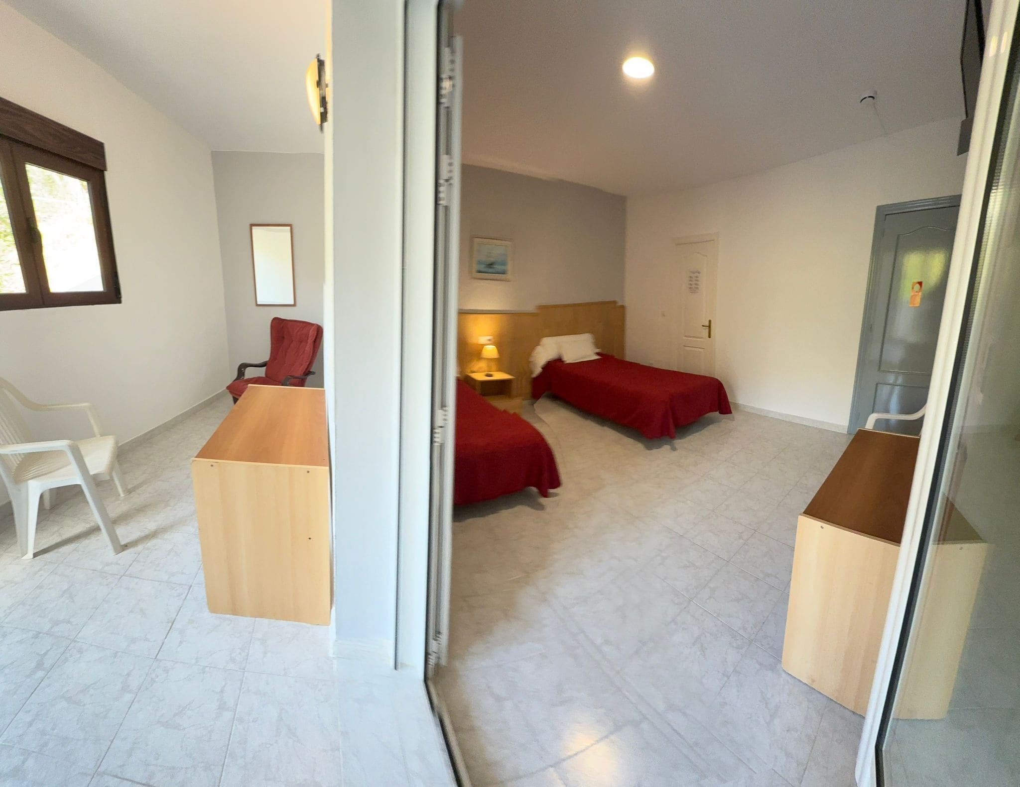 Una habitación con escritorio, dos camas, una silla y una ventana.