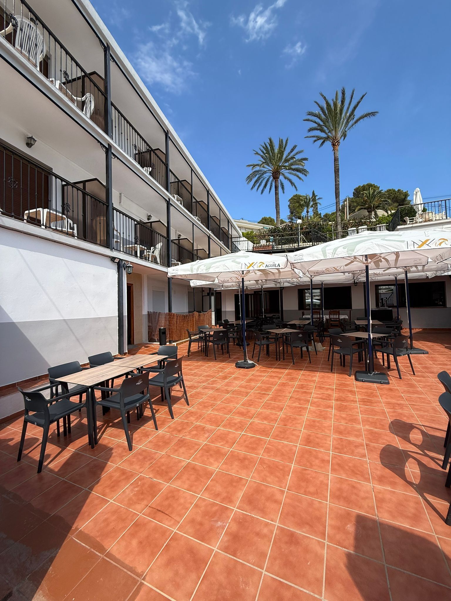 An outdoor patio with tables and chairs, a covered seating area, and a building with balconies.