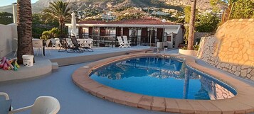 A swimming pool with lounge chairs, a patio area, and a view of a mountain and buildings.