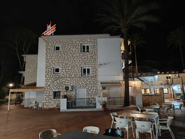 A stone building with a sign, outdoor seating, and palm trees. - Hotel Galera del Mar - Altea (Altea)