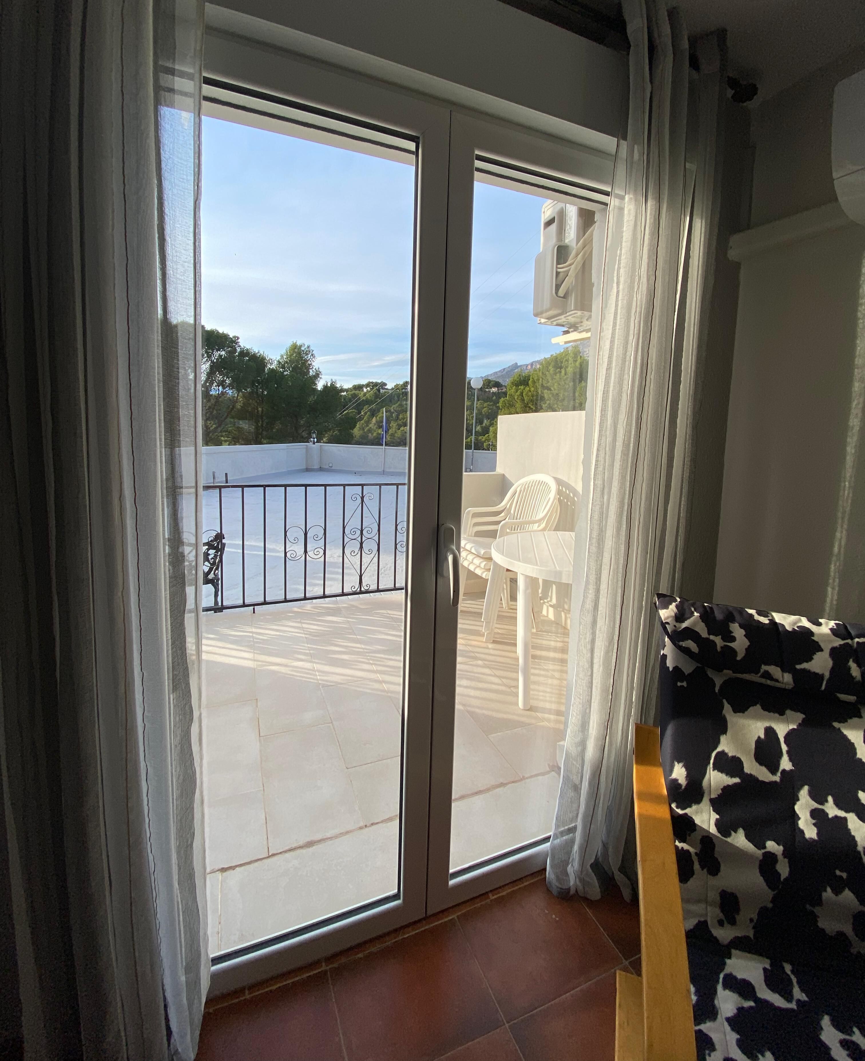 Una stanza con una porta a vetri scorrevoli che si apre su un balcone esterno con ringhiera in metallo e una sedia bianca.