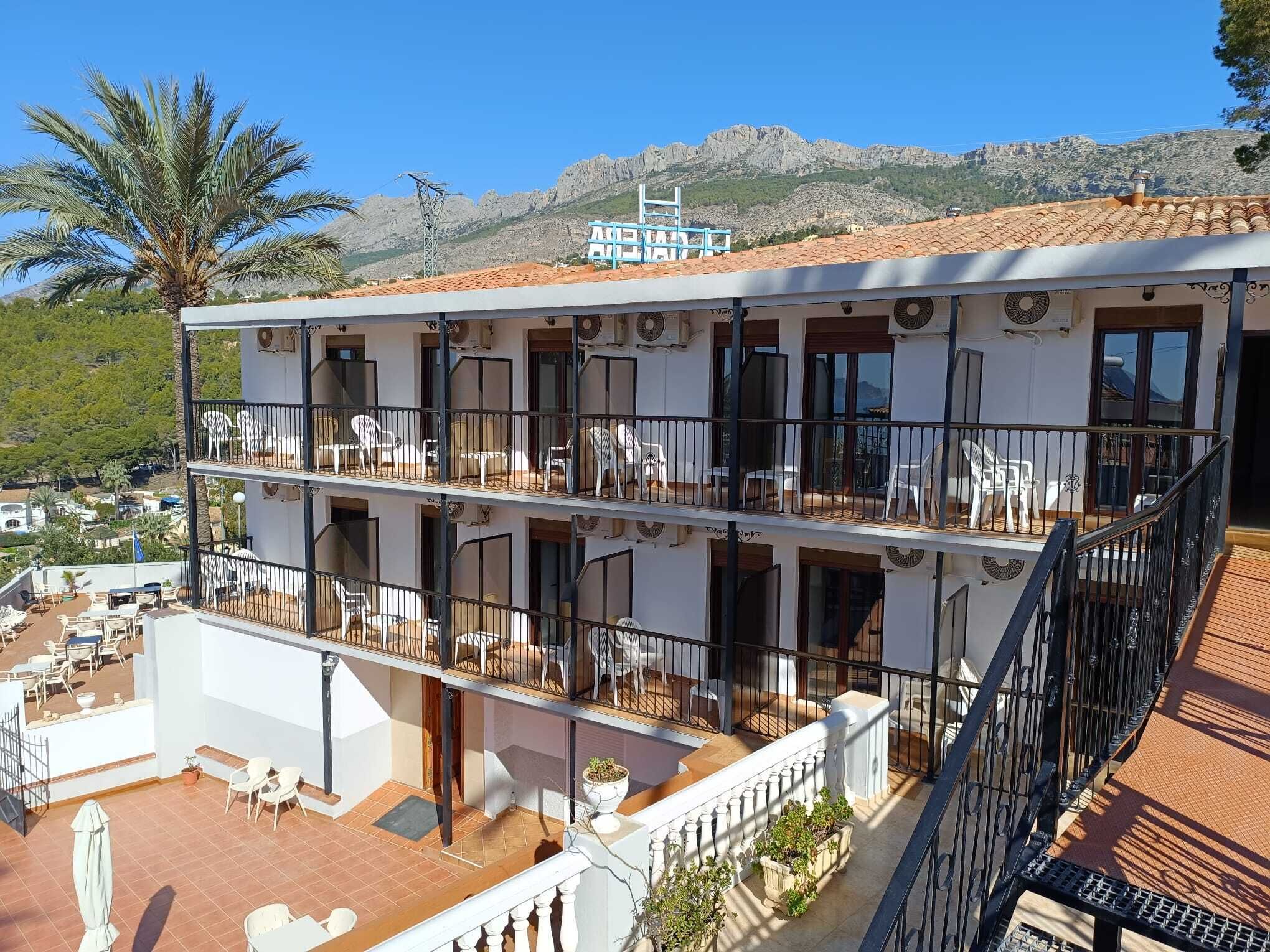 A multi-story building with balconies, outdoor seating, and a mountainous backdrop.