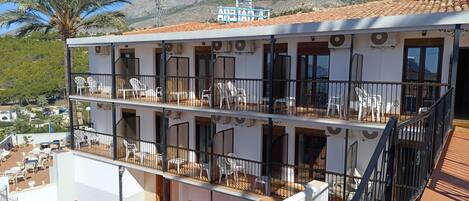 A multi-story building with balconies, outdoor seating, and a mountainous backdrop.