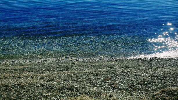 Una playa con agua cristalina, piedras y una isla en la distancia.