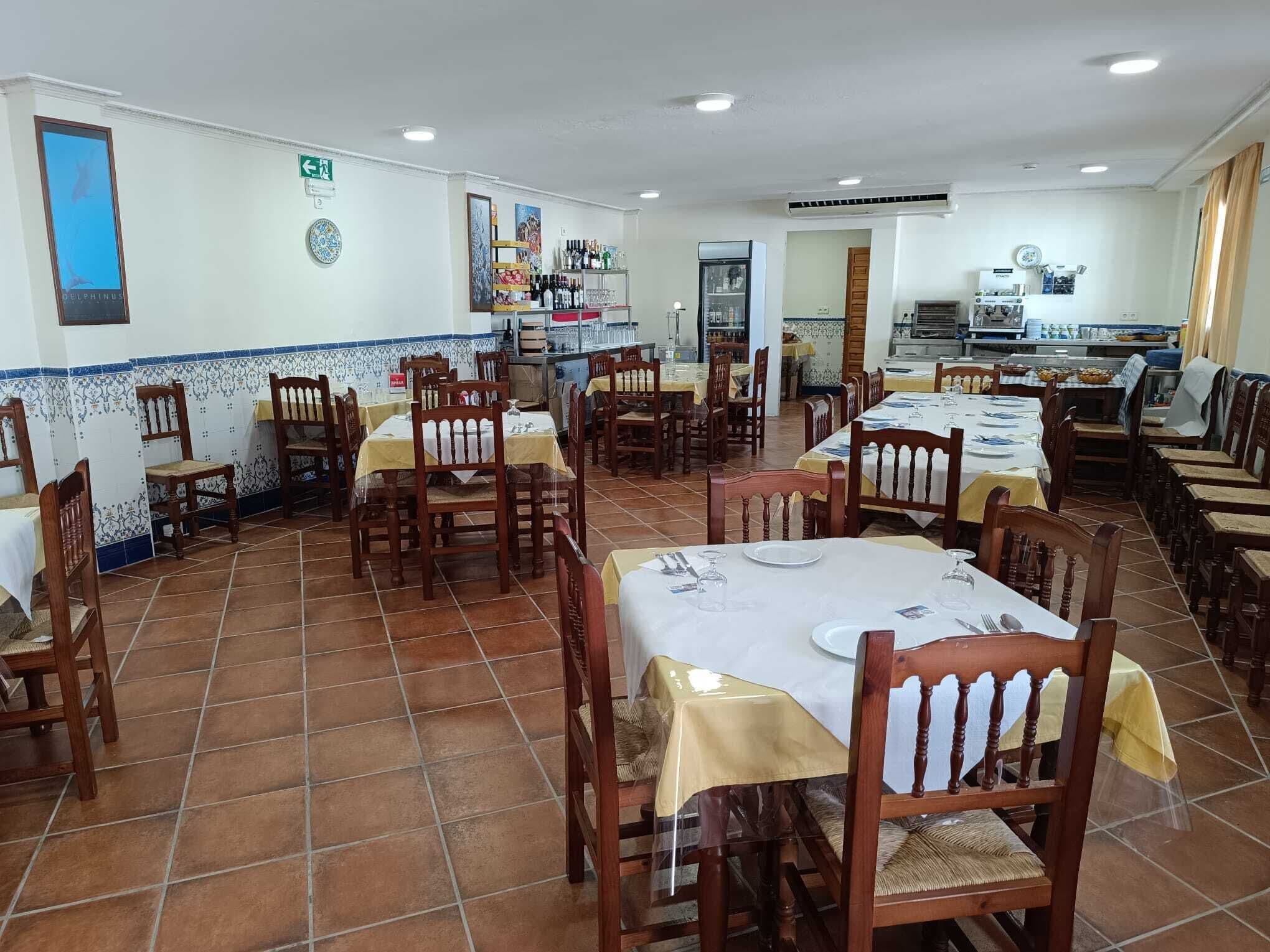 Un restaurante con varias mesas y sillas, una zona de cocina y un piso de baldosas.