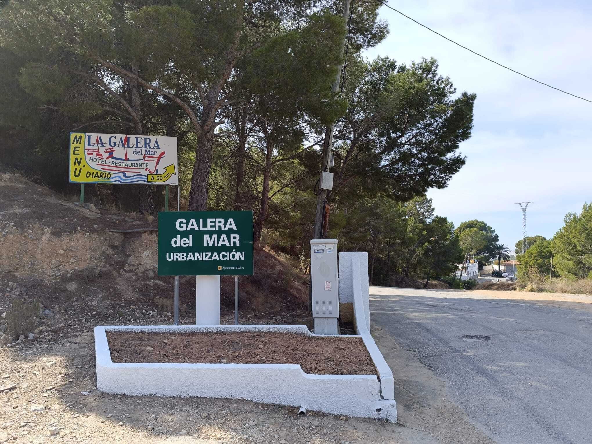 Placa indicando 'GALERA del MAR URBANIZACION', com uma trilha de terra e árvores ao fundo.