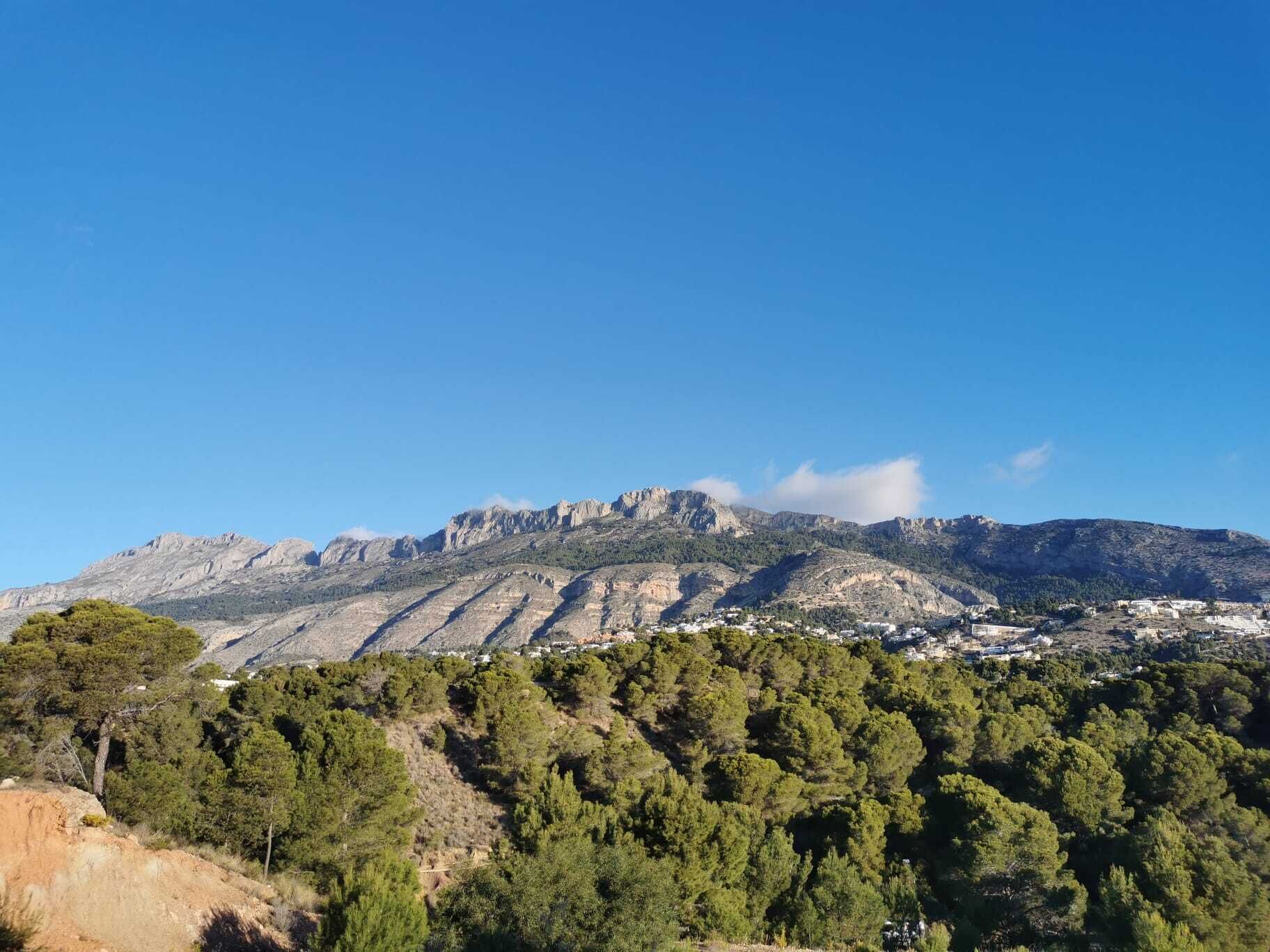 A mountainous landscape with a village at the base, clear skies, and dense forest.