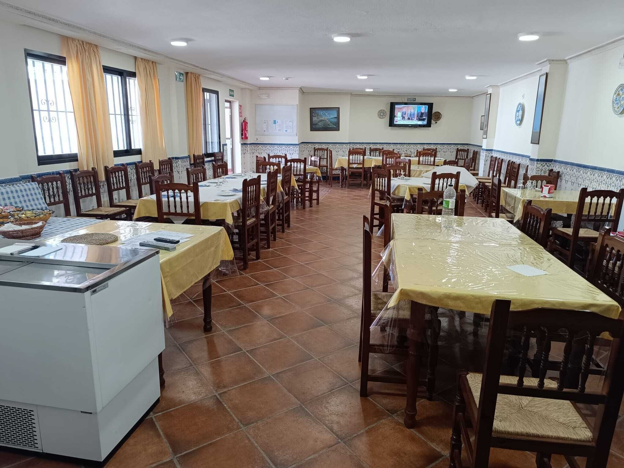A dining area with multiple tables and chairs, a kitchen counter, and a television mounted on the wall.