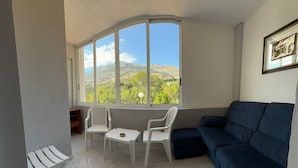 Una habitación con un ventanal curvo, un sofá azul oscuro, dos sillas blancas y una mesita.