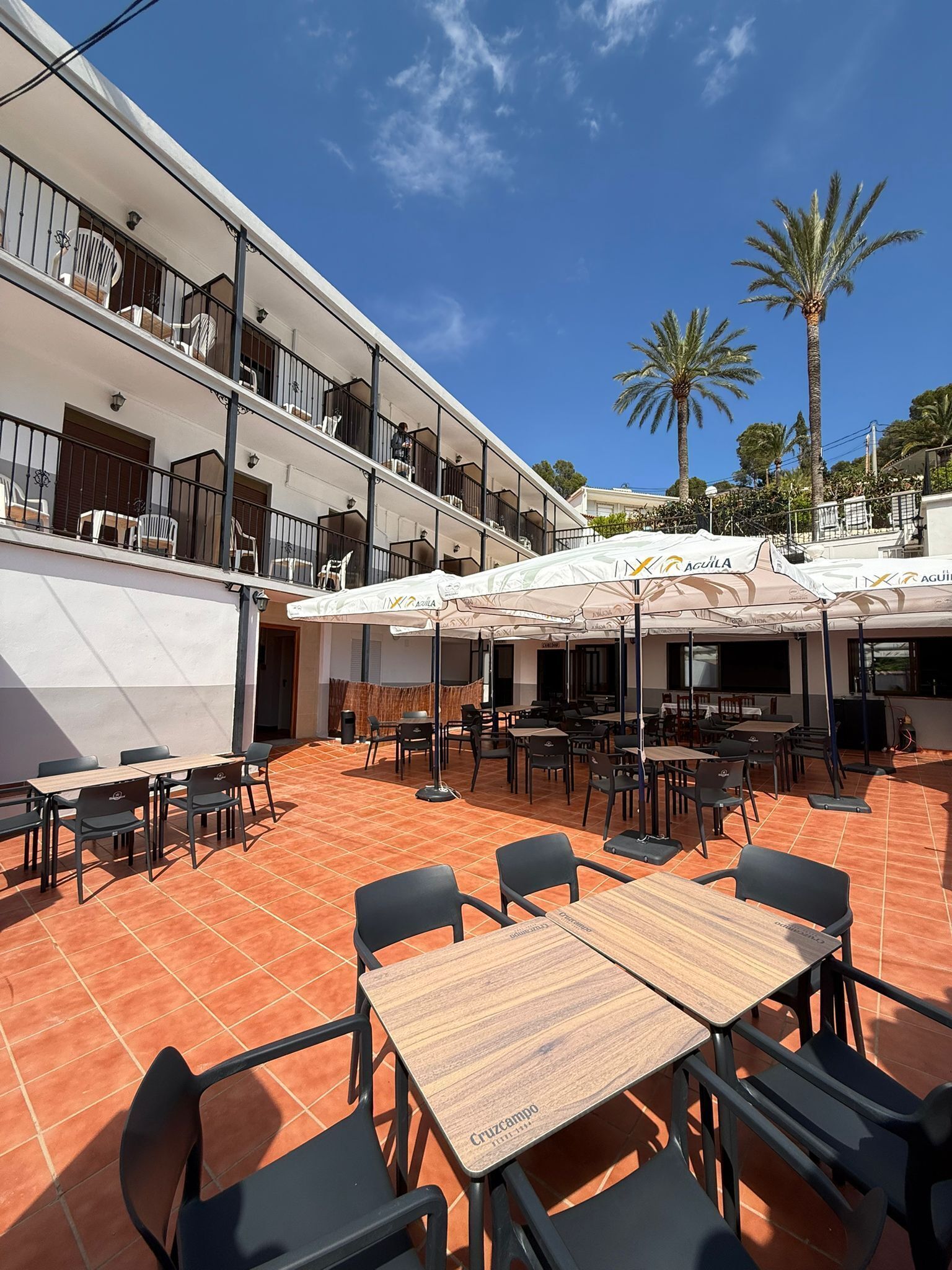 Une terrasse extérieure avec des tables et des chaises, un espace salon couvert et un bâtiment doté de plusieurs balcons.