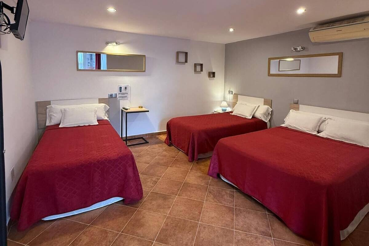 A hotel room with three beds, a desk, and a mirror.