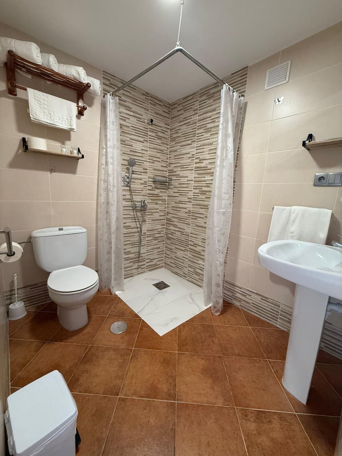 Baño con ducha, inodoro, lavabo y perchero para toallas.