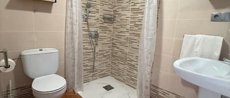 Baño con ducha, inodoro, lavabo y perchero para toallas.