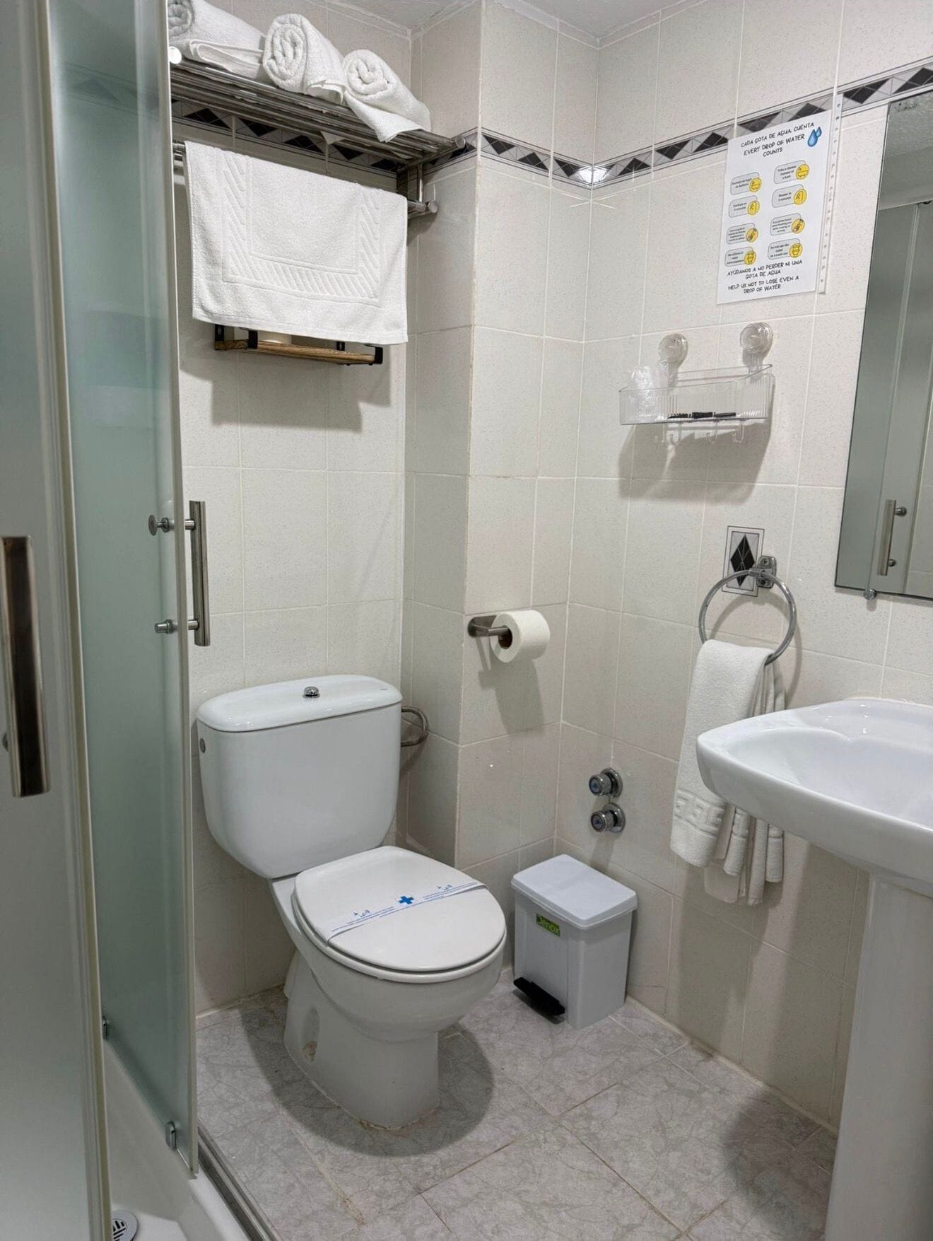 Un baño con inodoro, lavamanos, ducha y perchero para toallas.